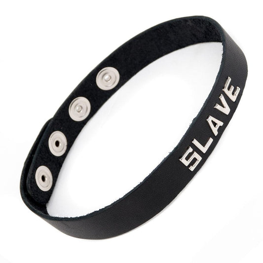 The Slave Black Leather Word Collar is displayed against a blank background. It is a thin strip of black leather with the word slave on the front in silver letters. The collar has snap closures in the back.