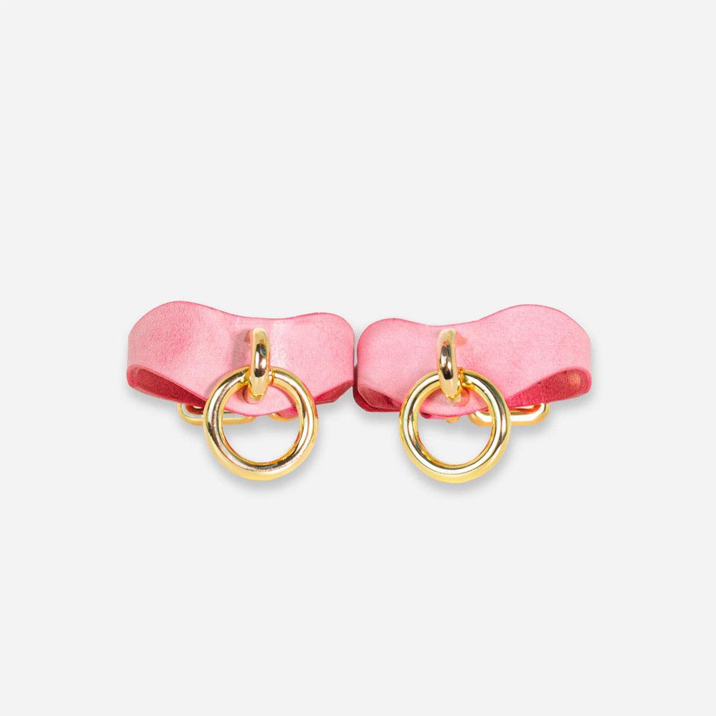 A pair of pink leather BDSM wrist cuffs on a white background, seen from the front. The attachment point is a gold-colored ring at the widest point.