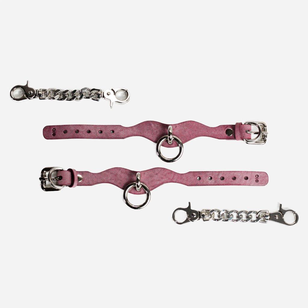 Two leather wrist cuffs opened full length on a white background. Next to them are two chains with crab-claw fasteners.