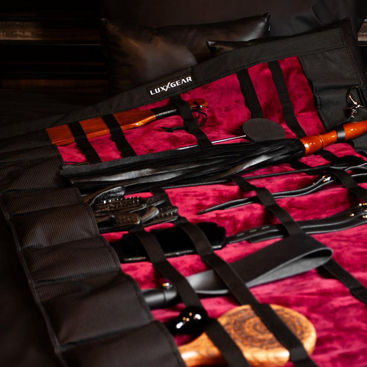 The KinkBag laid out flat with an assortment of toys in the pockets and straps. The inside is red cloth with a black exterior.