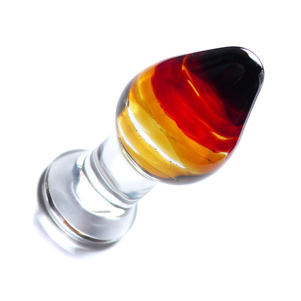 The Sun Glass Butt Plug is displayed against a blank background. The plug is tapered with a thin neck and wide base. The top of the plug is black, which fades into red, orange, and yellow as it goes down. The neck and base are clear.