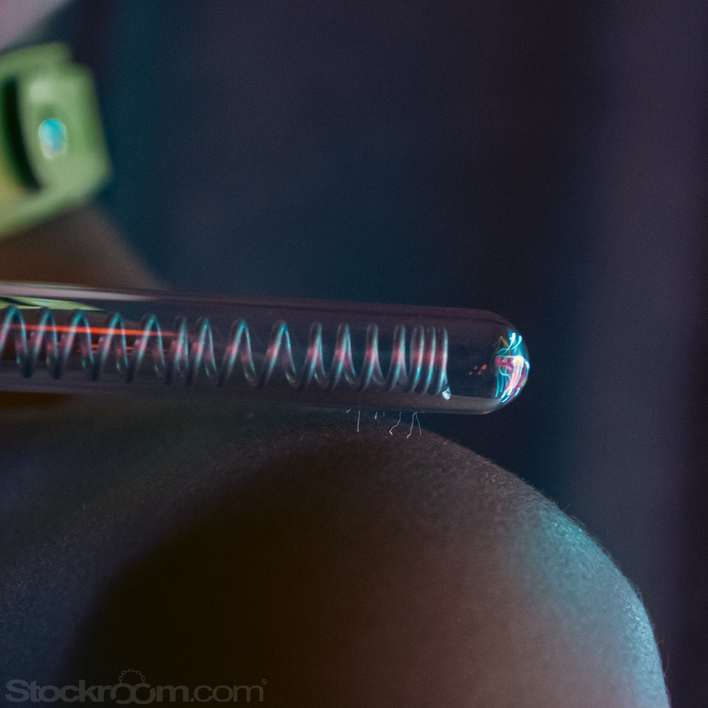 A close-up of a woman’s shoulder with the KinkLab Coiled Probe Neon Wand® Electroplay Attachment hovering over it is shown. There are tiny bolts of electricity coming from the probe and hitting her shoulder.