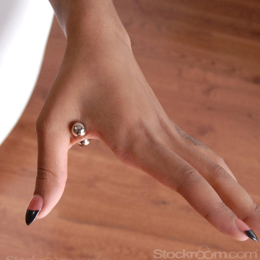 A close-up of a woman’s hand is shown with the web between her thumb and forefinger pinched between two Magnetic Nipple Balls.