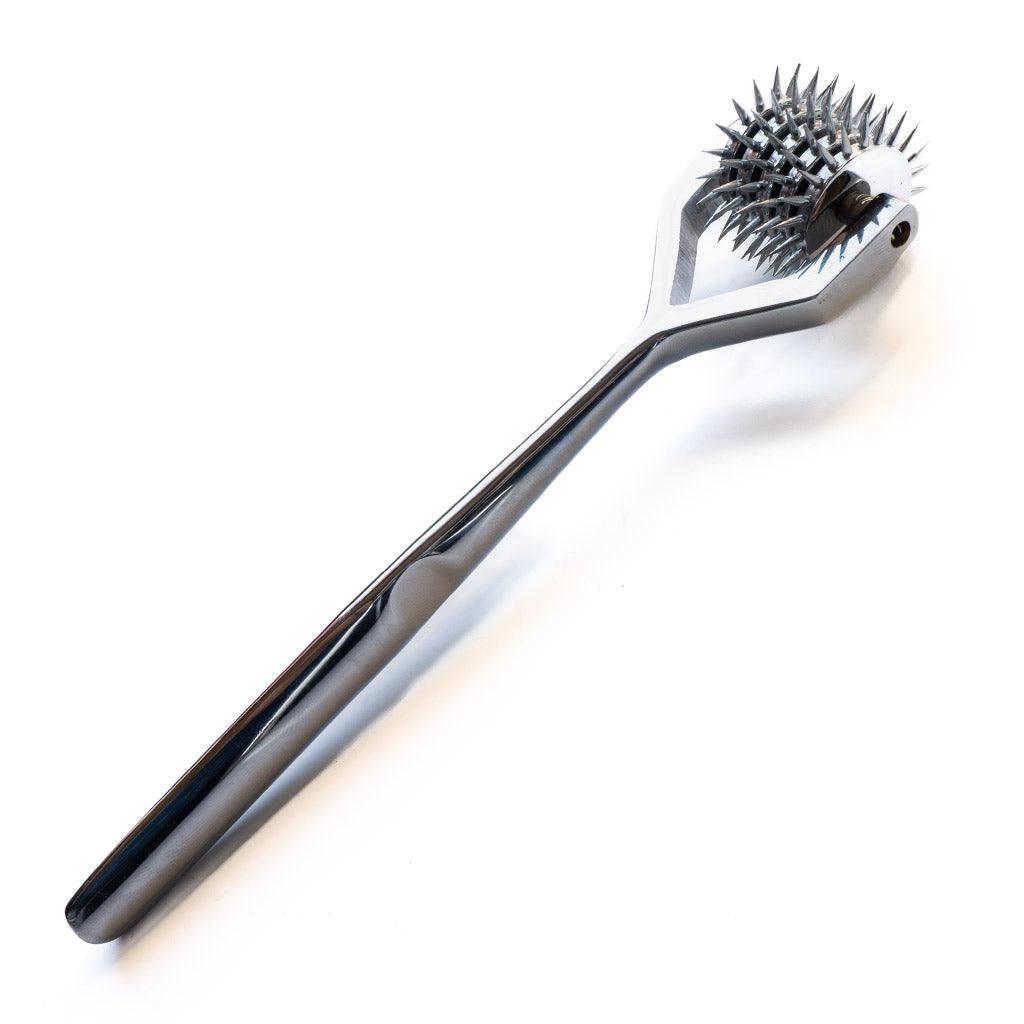 The 5 Wheel Pinwheel is displayed against a blank background. The wheel is made of silver metal and has a long, thin handle with the wheel at one end. The wheel has five rows of spikes.