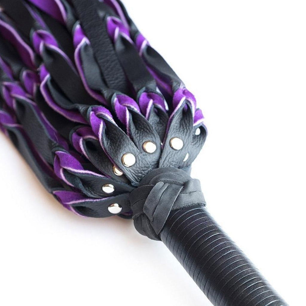 A close-up of the top of the purple and black Braided Leather Flogger handle is displayed against a blank background.