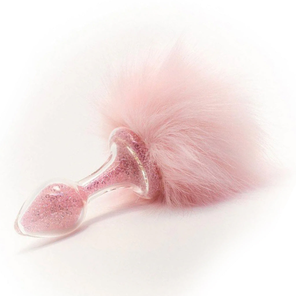 The Pink Magnetic Sparkle Bunny Tail Glass Butt Plug is shown against a blank background. The butt plug is filled with pink glitter, and a puff of pink fur is attached to the base of the plug.