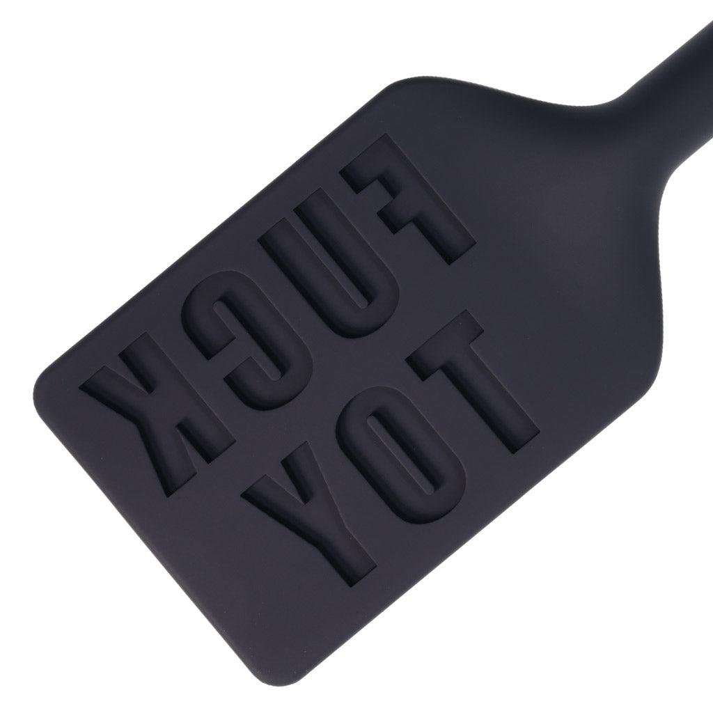 A closeup of the top end of the black silicone paddle. The words "FUCK TOY" are inscribed backwards in the surface.