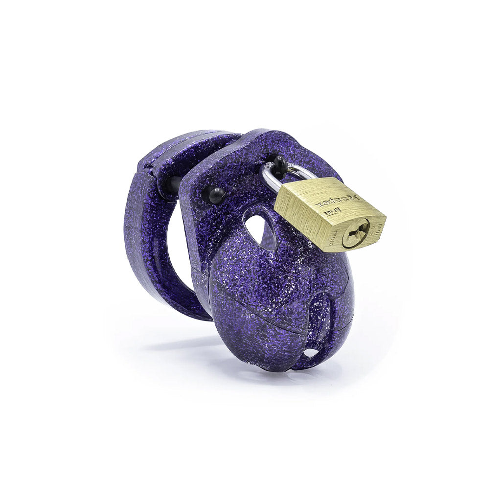 The CBX "Mini-Me" penis cage, shown on a white background. The cage is made of purple plastic with a glittery surface. A brass padlock holds the top closed.