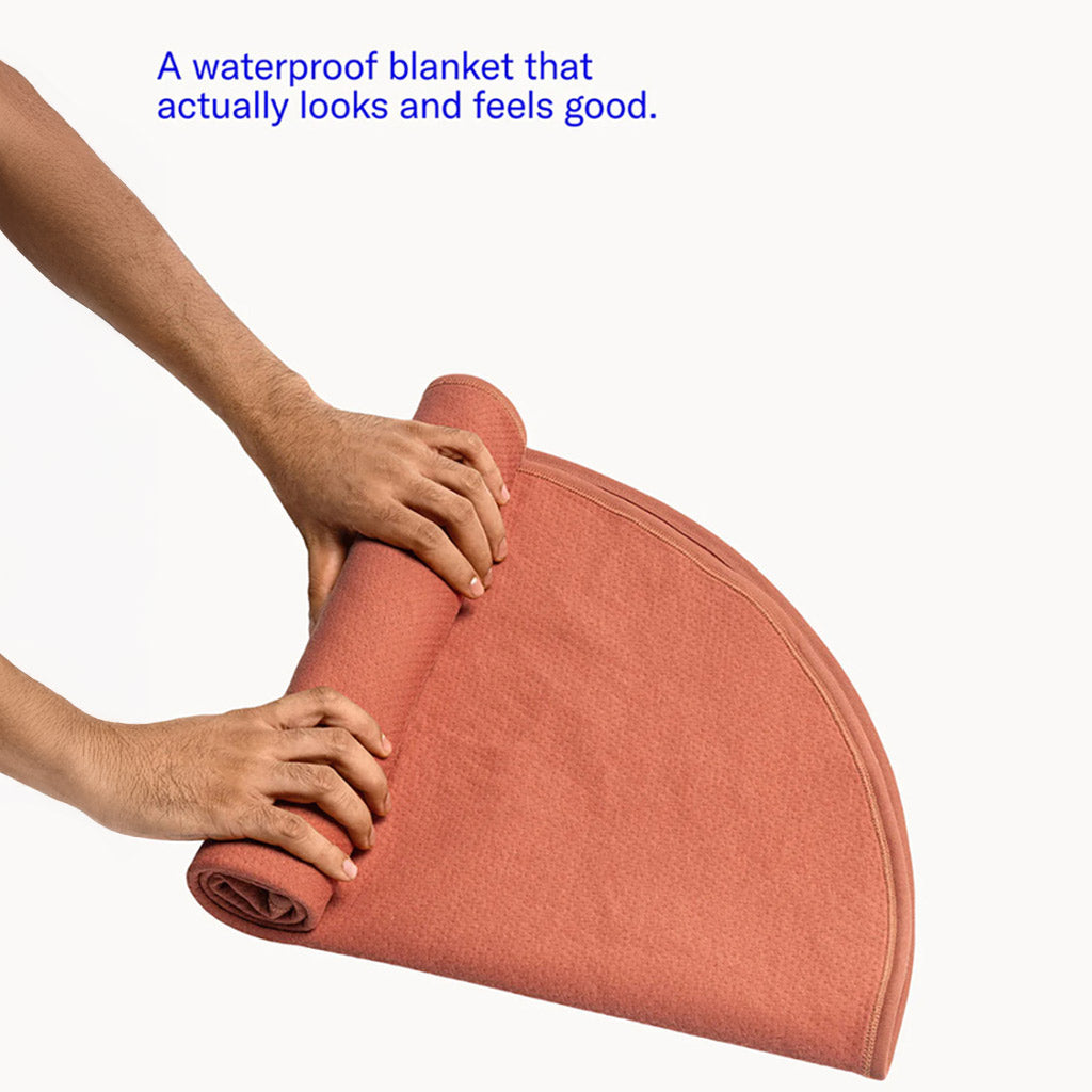 Text: "A Waterproof blanket that actually looks and feels good." Two hands are shown folding and rolling up the blanket.