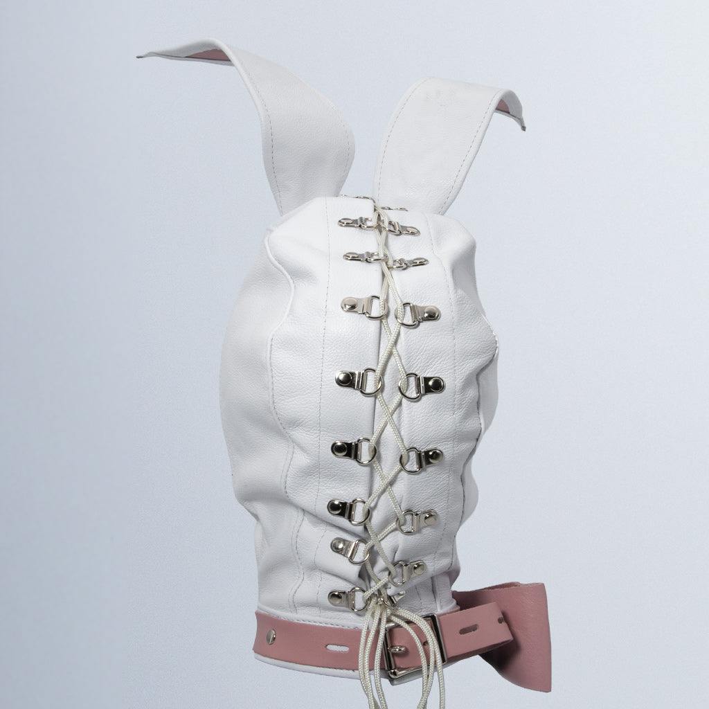 The white Leather Bunny Hood is shown on a blank background from behind. The back has silver metal rivets going down in a vertical line with white leather laces tied through them. The base of the hood has an adjustable pink leather collar with a bow on the side.