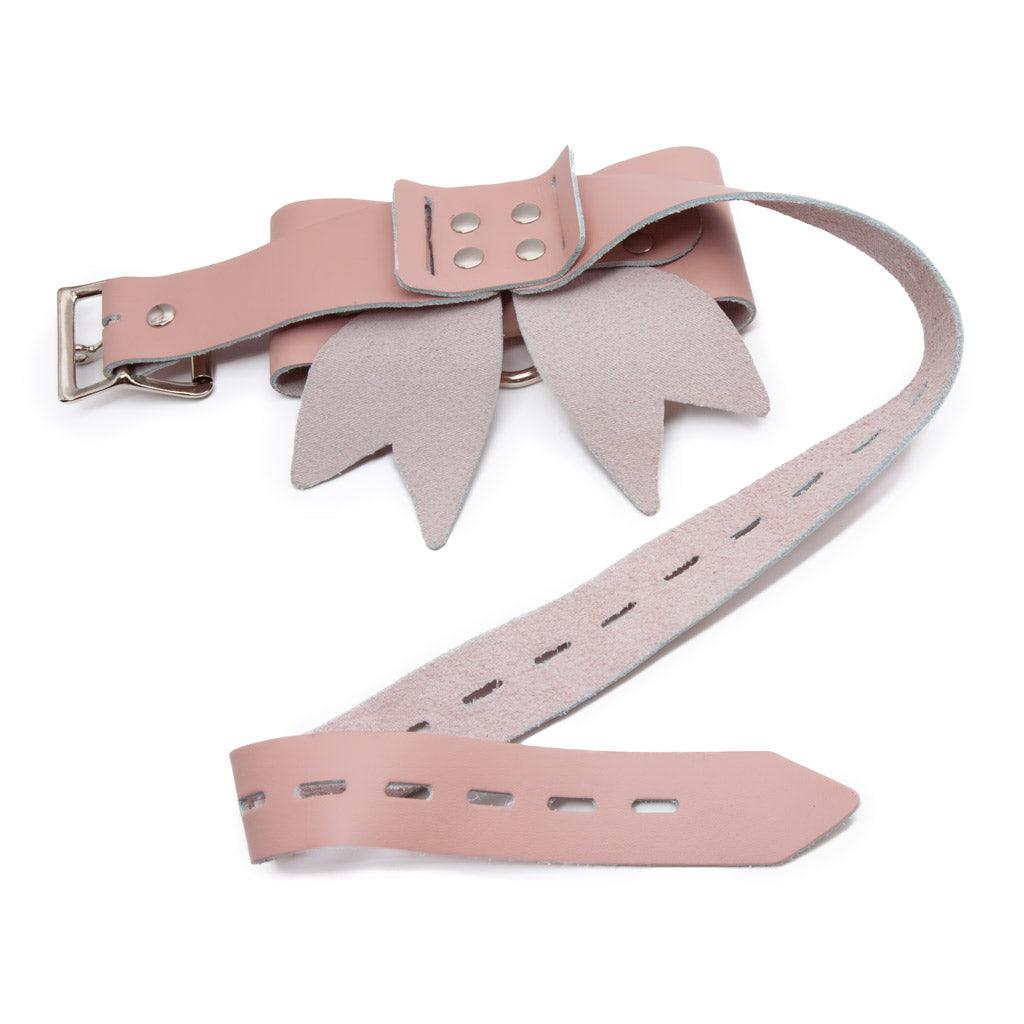 A leather bow seen from behind, with the strap unfastened to show the adjustable holes. Small silver fasteners stand out against the powder-pink leather.