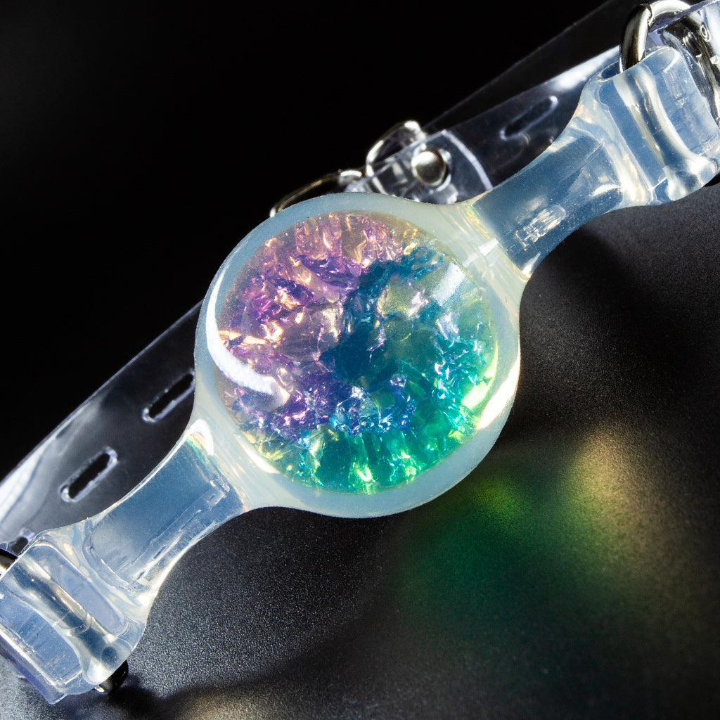 Close-up of a transparent PVC ball gag, showing the glittery purple, yellow, and green materials inside the ball.