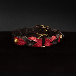 The Melanie Rose Designs x The Stockroom Collar, made of red and black leather braided together with a gold O-ring in the center, is displayed against a black background.
