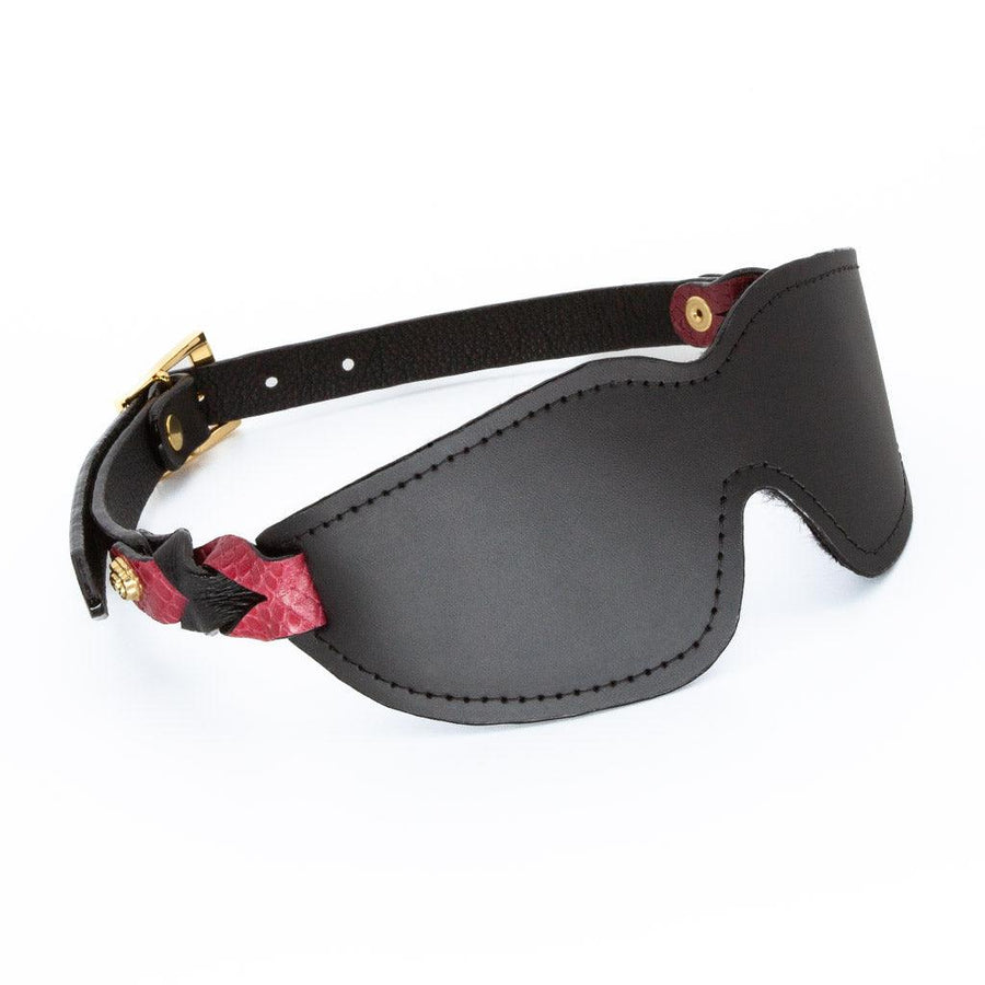 The Melanie Rose Designs x The Stockroom Blindfold, a black leather blindfold with straps made of braided black and red leather, is displayed against a blank background.