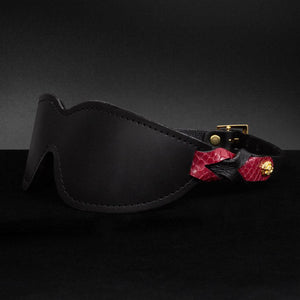 The Melanie Rose Designs x The Stockroom Blindfold, a black leather blindfold with straps made of braided black and red leather, is displayed against a black background.
