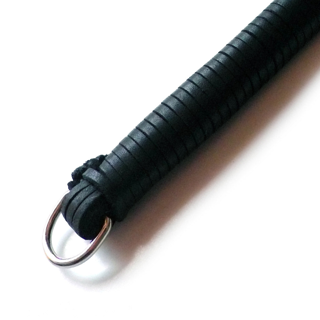 A close-up of the black leather 20-inch Thong Whip with Spiked Tails leather-wrapped handle with a D-ring at the end is displayed against a blank background.