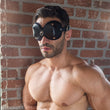 Load image into Gallery viewer, A shirtless, muscular brunette man with light facial hair poses next to a brick wall, wearing the black Mistress Heather Leather Blindfold.