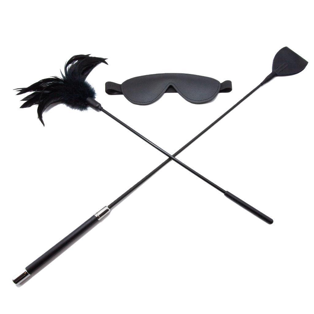 Some of the contents of the Bondage 101 Kit made by The Stockroom are shown on a white background. Shown in this image is the black riding crop with wide end, black leather blindfold, and black feather tickler.