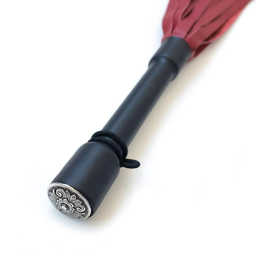 A close-up of the Red Devil Leather Flogger By Dragontailz handle is displayed against a blank background, showing the silver ornamental cap on the end of the handle.