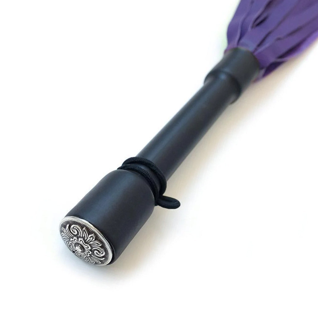 A close-up of the Purple Devil Leather Flogger By Dragontailz handle is displayed against a blank background, showing the silver ornamental cap on the end of the handle.