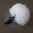 Load image into Gallery viewer, The White Rabbit Fur Bunny Tail Silicone Butt Plug is displayed against a gray background. The plug is made of matte black silicone and is small and tapered with a thin neck and wide base. Attached to the base is a large puff of white fur.