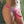 Load image into Gallery viewer, A close-up of a woman&#39;s hips is shown in front of a green wall. She wears The Betty Strap-on Harness with a pink dildo attached. There is a small red ribbon bow attached to the harness right above the dildo.
