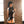 Load image into Gallery viewer, A woman with black hair stands facing a brick wall while looking over her shoulder. She is holding the 24&quot; Basic Suede Flogger with the falls draped over her shoulder. She is wearing a latex bra, panties, garter belt, and thigh highs, all in black.
