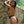 Load image into Gallery viewer, A nude woman with light brown hair faces a stone wall outdoors, bracing herself against the wall with her forearms. She is looking over her shoulder at the Deluxe Locking Chastity Belt that she is wearing, which is padlocked right above her butt.
