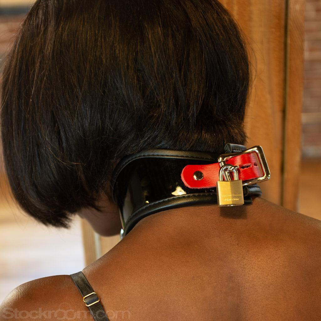A close-up of the back of a woman's neck is shown. She wears the Firecracker Patent Leather Posture Collar, which has an adjustable red strap and a lockable buckle. The buckle has a brass padlock on it.