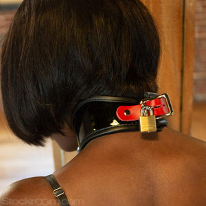 A close-up of the back of a woman's neck is shown. She wears the Firecracker Patent Leather Posture Collar, which has an adjustable red strap and a lockable buckle. The buckle has a brass padlock on it.