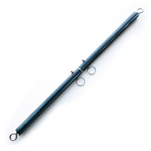 The Leather Wrap General Purpose Spreader Bar is shown against a blank background. It is a thin pole covered in black leather. At each end of the bar is a metal eyebolt. In the middle are two metal pins that can be moved to adjust the bar’s length.