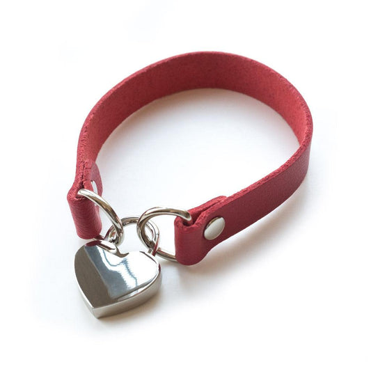 A red leather choker on a white background. Two D-rings are held closed with a heart-shaped padlock.