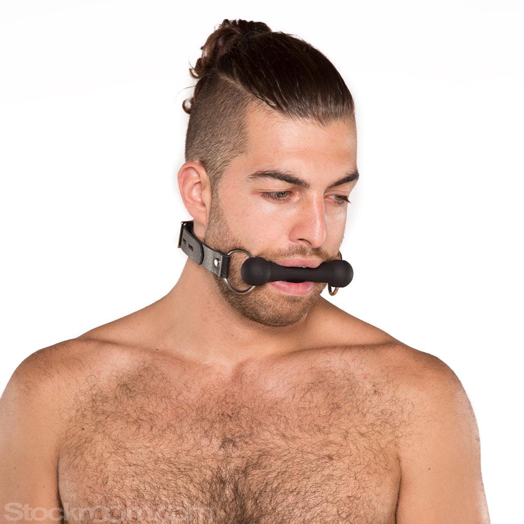 A man with dark brown hair that is shaved on the sides and pulled into a ponytail is shown wearing the Kinklab Silicone Bit Gag against a blank background.