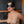 Load image into Gallery viewer, A nude woman with dark hair and bright red lipstick is standing against a black wall. Her eyes are covered by the Adjustable Blindfold, which is made of black leather and shaped like an infinity symbol.
