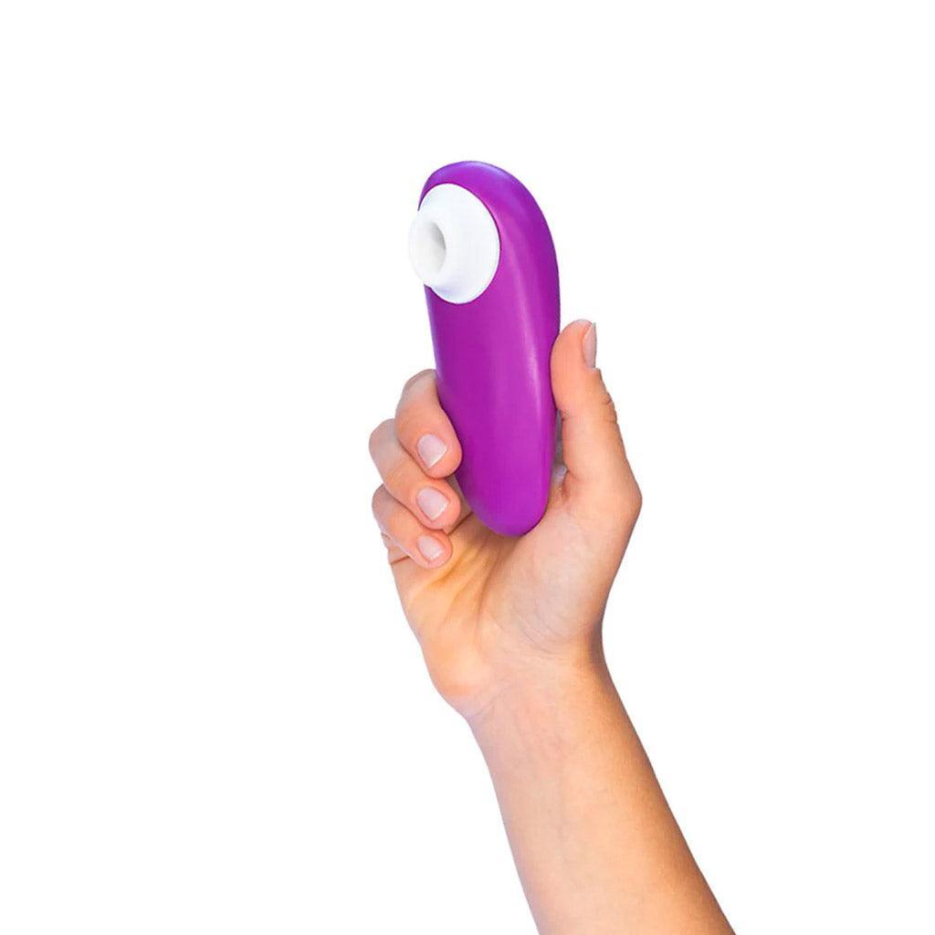 A hand is shown holding a Womanizer Starlet 3 vibrator in Violet up against a blank background.