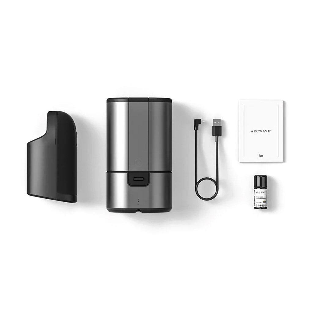 The contents of the Arcwave Ion Pleasure Air Masturbator package are shown against a blank background. This includes the masturbator, a charger and storage case, the manual, and a small bottle of lube.