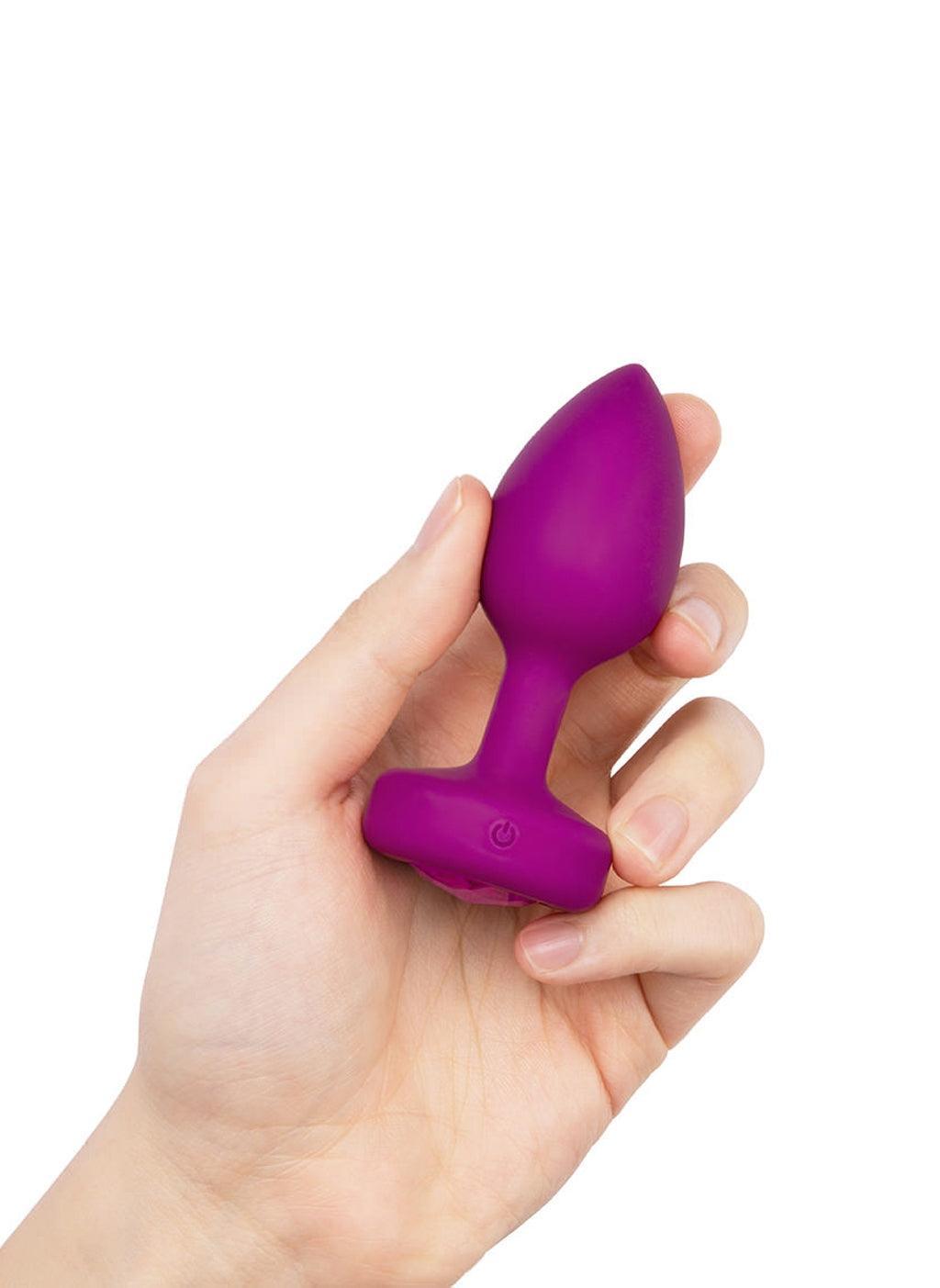 A hand is shown holding up the b-Vibe Vibrating Jewel Butt Plug in Fuchsia against a blank background.