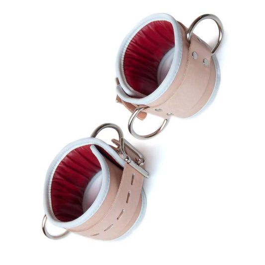 The Deluxe Padded Medical Leather Ankle Restraints are shown against a white background. The cuffs are made of tan leather with a white border and a red inner lining. They have metal hardware.The Deluxe Padded Medical Leather Ankle Restraints are shown against a blank background. The cuffs are made of tan leather with a white border and a red inner lining. They have metal hardware.