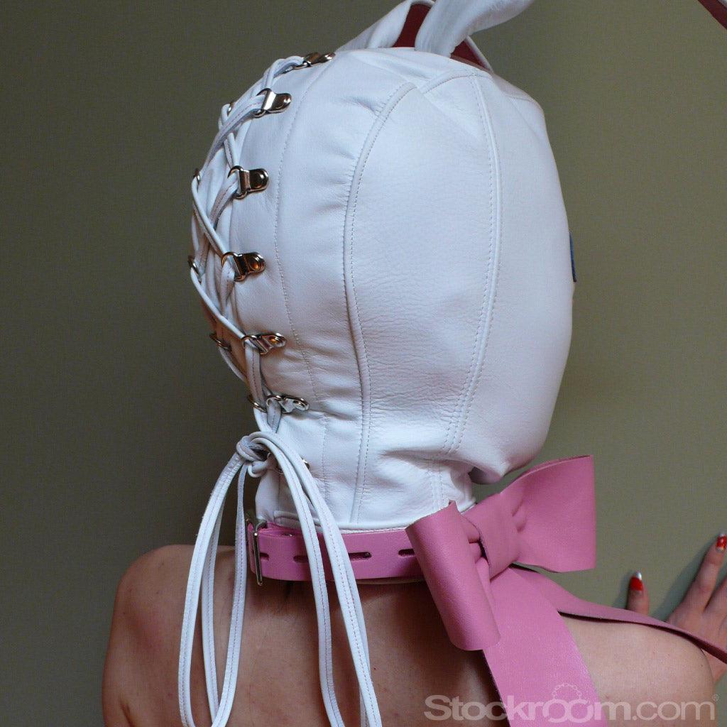 The white Leather Bunny Hood is shown on somebody’s head from behind. The back has silver metal rivets going down in a vertical line with white leather laces tied through them. The base of the hood has an adjustable pink leather collar with a bow on the side.