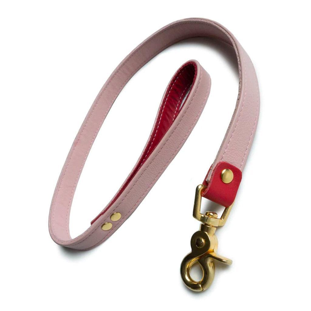The Premium Garment Leather Leash with 18k Gold Plated Hardware is shown against a white background. The leash is made of a light pink leather strip with red accents and has a wrist loop on one end and a gold snap hook on the other.
