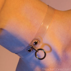 A close-up of a woman's bare neck in pinkish-purple lighting is shown. She wears the Clear CTRL Vinyl Choker.