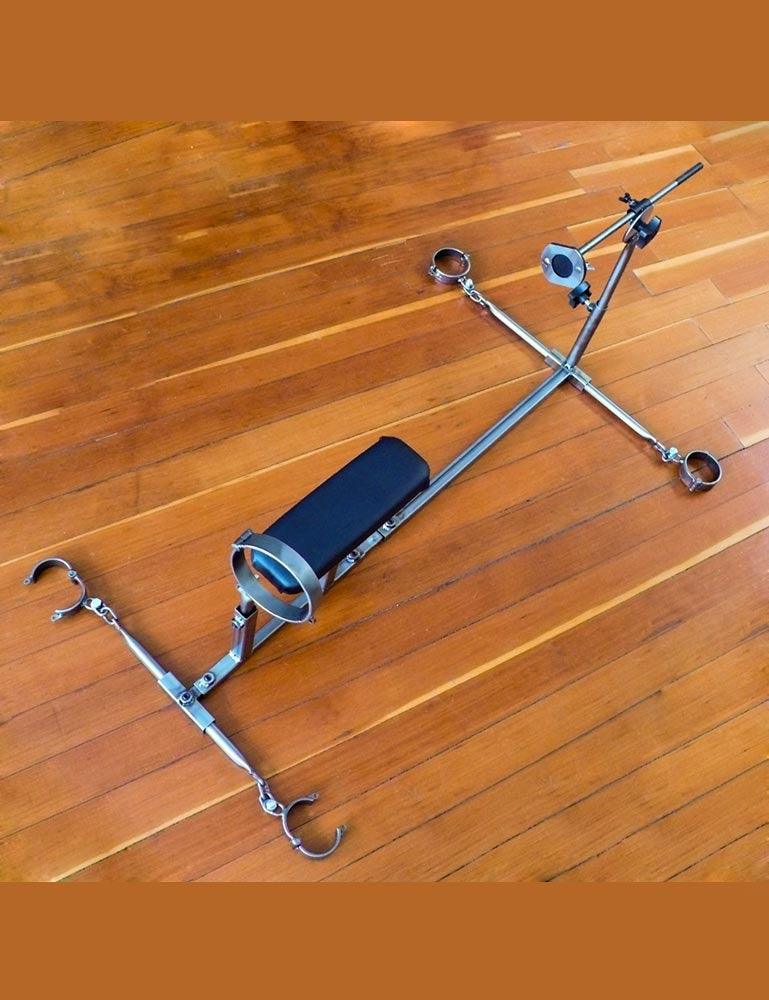The Stockroom Stockade is shown on a wooden floor. It has 1 vertical bar with 2 horizontal spreader bars with metal cuffs. It has an upright bar with a metal collar and a fucking rod at the other end. The leather stomach support is not upright.