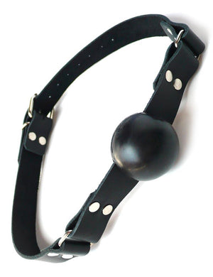The black rubber ball gag is displayed against a blank background. It is a matte black rubber ball attached to a black leather strap with silver hardware, which buckles behind the head.