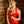 Load image into Gallery viewer, A woman with short, curly brown hair stands in front of a wooden door, wearing a red Syren latex dress. She holds the Brown Leather Heart Crop in front of her with both hands.
