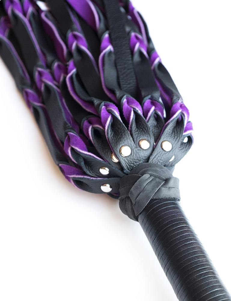A close-up of the top of the purple and black Braided Leather Flogger handle is displayed against a blank background.