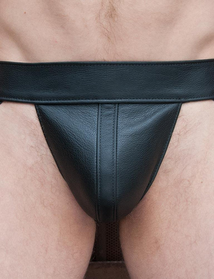 A close-up of a man's groin is shown. He wears the black Leather Jockstrap from The Stockroom.