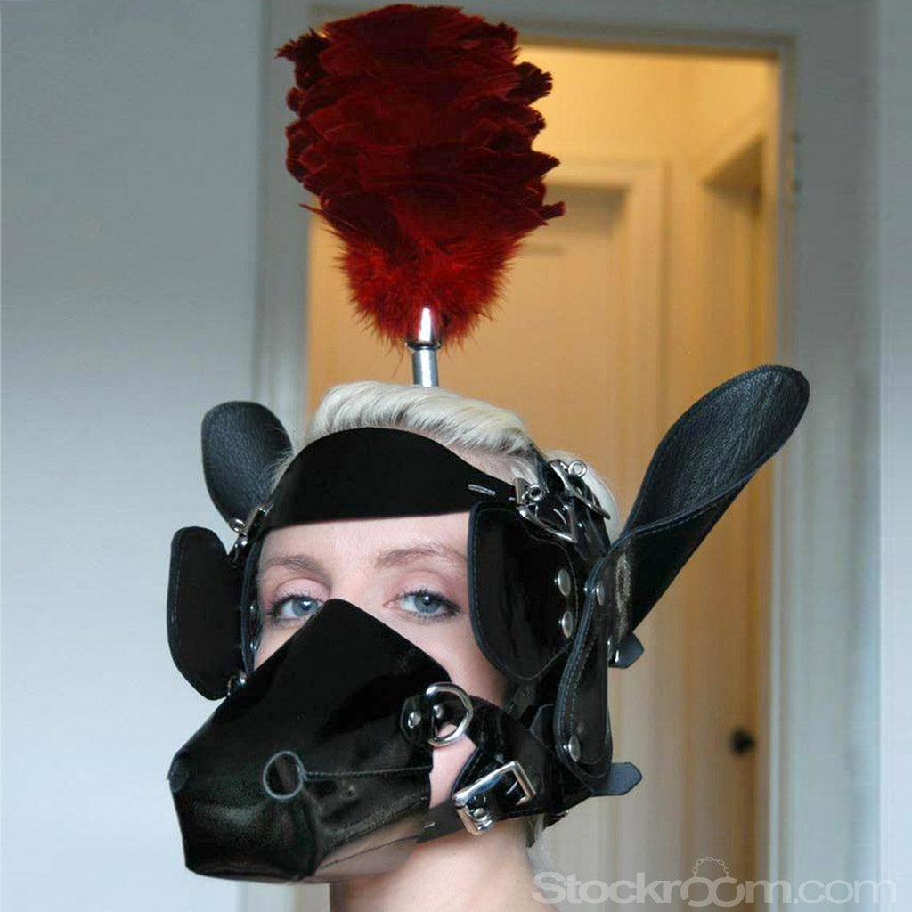 A close-up of a woman's head is shown. She wears the Patent Leather Pony Head Bridle w a red feather Plume. The mask is shaped like a horse's muzzle that covers her mouth, and horse ears are attached to the side of her head.