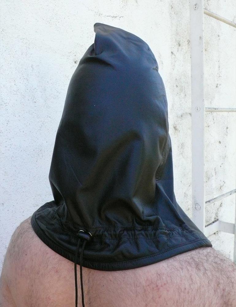 A man standing against a white wall is shown from behind, wearing the Leather Guillotine Hood. The base of the hood hits the top of his back. There is an adjustable drawstring cord near the base of the hood.
