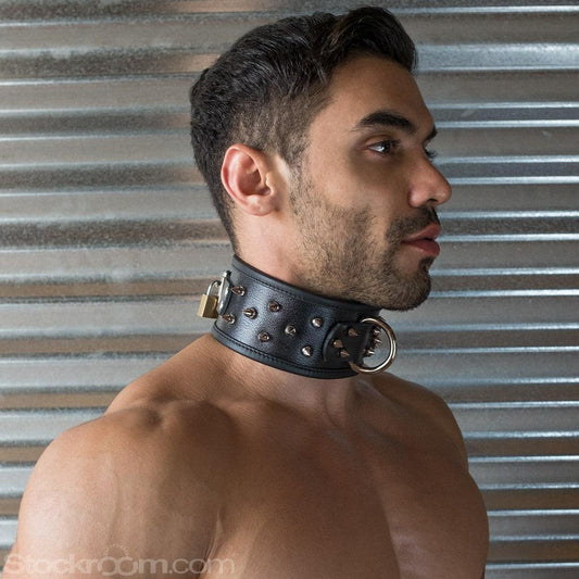 A close-up of a brunette man with facial hair is shown in profile. He wears the BDSM Alpha Dog Leather Collar with Spikes. The collar is wide and has a metal D-ring in the center and spikes covering it. It is padlocked in the back.