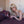 Load image into Gallery viewer, A blonde woman in a silver bra with long red nails holds the Kinklab Viberite® Cordless 7 Speed Personal Wand Massager. She is lying on her stomach on a bed with burgundy sheets.
